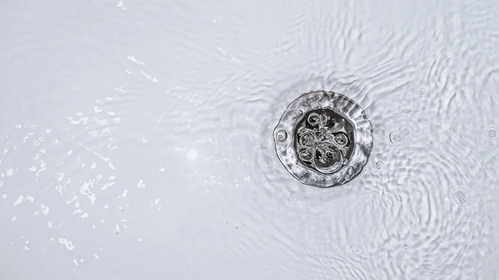 Close-up of a drain opening with water ripples across the surface. Slow draining water.