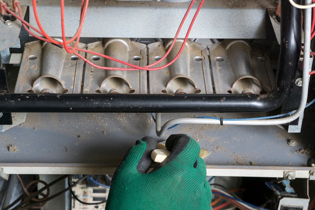 Technician inspecting or servicing gas furnace burners inside a residential heating system. Best for blogs about furnace maintenance, furnace cleaning, burner cleaning, heating tune-ups, furnace service checklist, and why annual furnace maintenance matters.